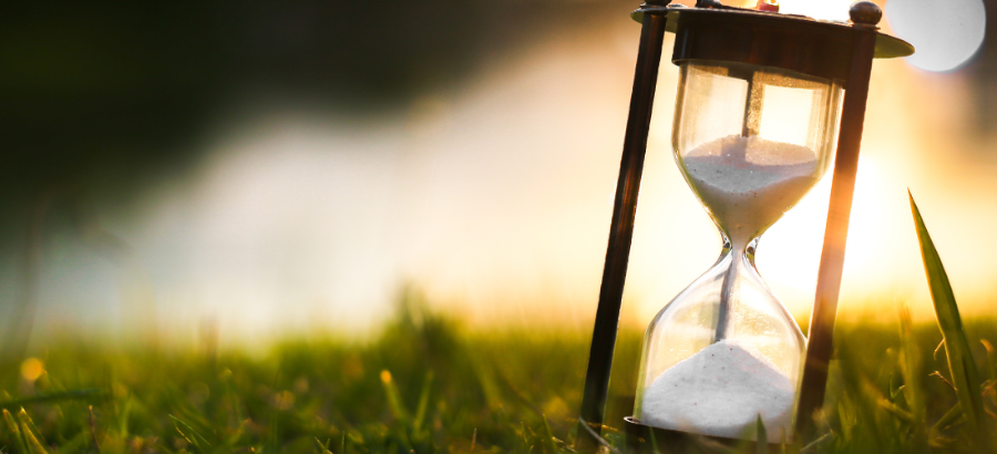 An hourglass in a field in front of a sunset.